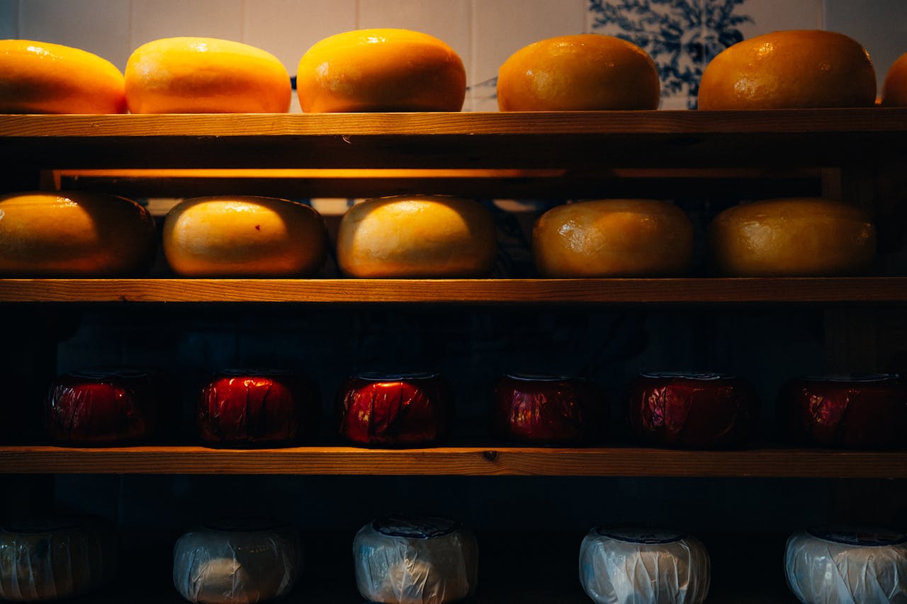 about-us A variety of Gouda and Edam cheese wheels displayed on wooden shelves in Amsterdam.