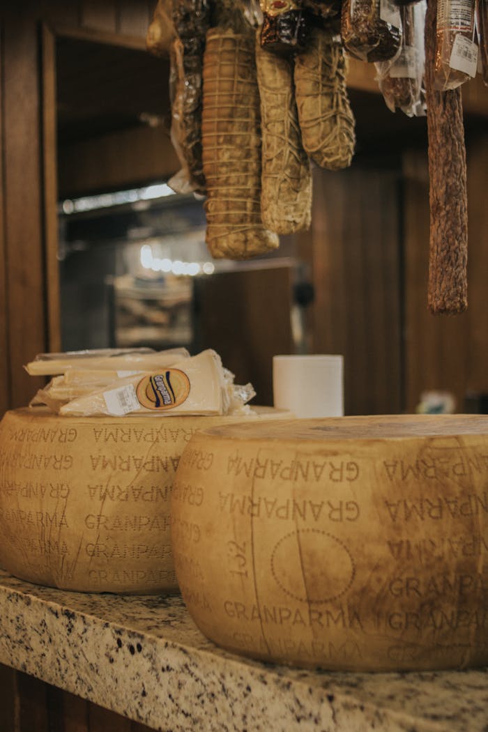 services-03 Aged Gran Parma cheese wheels displayed in a rustic market with cured meats.