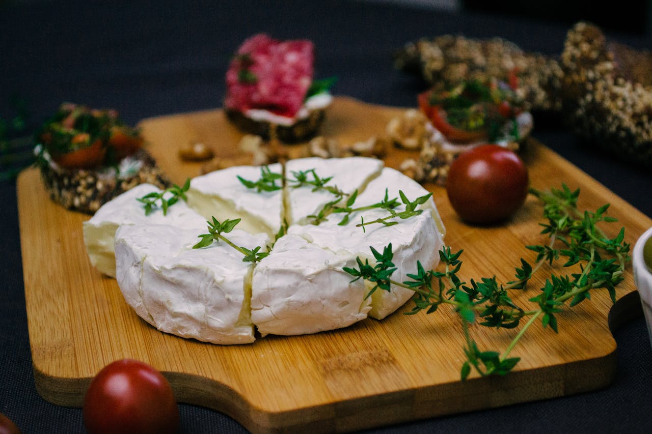 services-04 Appetizing cheese platter featuring camembert, herbs, and fresh tomatoes on a wooden board.